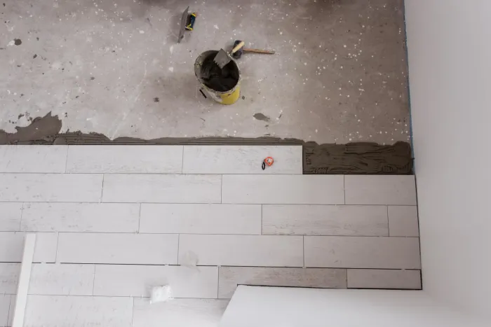 Artisan posant du carrelage grand format dans une salle de bain en rénovation en Gironde